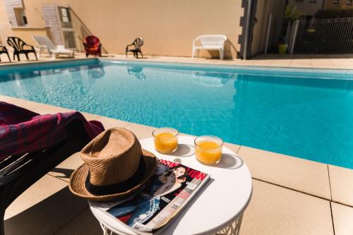 a hat and two glasses of orange juice on a table by a pool at Garden & City Clermont-Ferrand - Gerzat in Gerzat