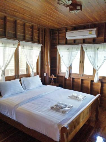 a bedroom with a bed with white sheets and windows at Huanmaisakngam Resort in Ban Buak Khang