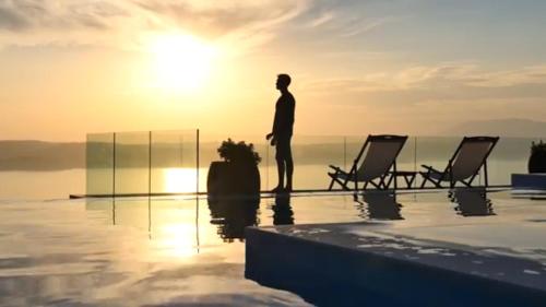 a man standing on the edge of a swimming pool with the sunset at Villa Salina Luxury Pool Villa in Kechria