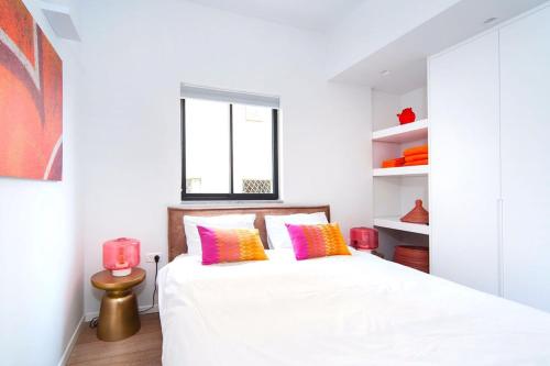 ein Schlafzimmer mit einem weißen Bett mit rosa und gelben Kissen in der Unterkunft Frishman Dream by Five Stay in Tel Aviv