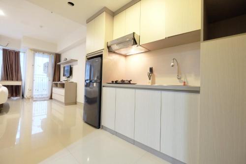 a kitchen with white cabinets and a black refrigerator at Best Price Modern Studio Apartment H Residence near MT Haryono By Travelio in Jakarta