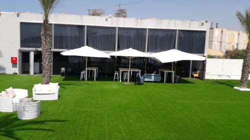 a lawn with white chairs and umbrellas in front of a building at El Yam in Netanya