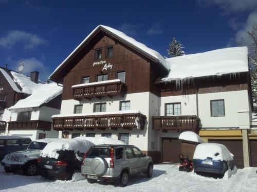 a snow covered building with cars parked in front of it at Pension Luky in Špindlerův Mlýn
