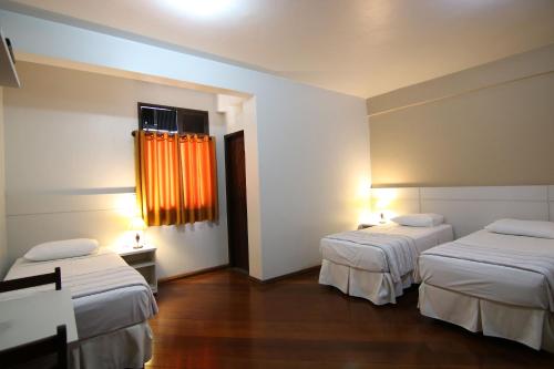 Habitación con 2 camas y ventana con cortinas de color naranja. en Samba Betim en Betim