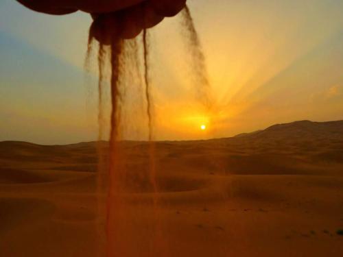 a sunset in the desert with the sun in the distance at Berber Camp in Merzouga