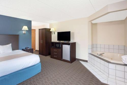 a hotel room with a bed a tub and a television at AmericInn by Wyndham Green Bay West in Green Bay