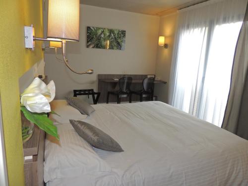 a bedroom with a white bed with a table and chairs at The Originals Boutique, Hôtel La Chaussairie, Rennes Sud in Chartres-de-Bretagne
