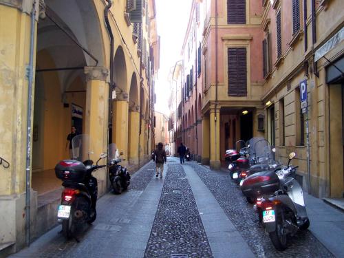 a row of motorcycles parked on a narrow street at Enjoy Bologna Apartment in Bologna