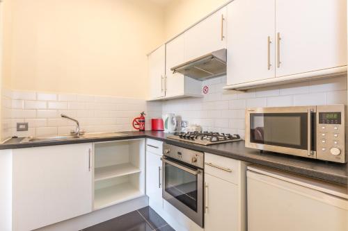cocina con armarios blancos y microondas en Menzies Apartments, en Edimburgo