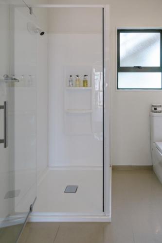 a white bathroom with a shower and a toilet at Blue Marlin Apartments in Whitianga