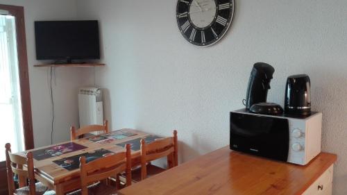 a dining room table with a microwave and a clock on the wall at Charmant T2 avec cabine fermée et terrasse in Les Angles