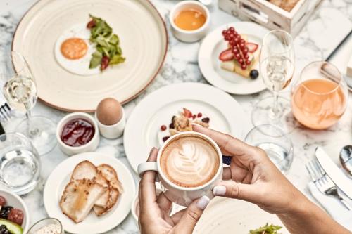 a person holding a cup of coffee at a table with food at Antigon Urban Chic Hotel, Thessaloniki in Thessaloniki