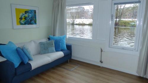 a living room with a blue couch and two windows at Houseboat In The Center, 5 min walk to Tropical Museum, Free Wifi! in Amsterdam