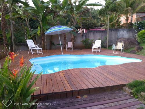einen Pool mit Stühlen und einem Sonnenschirm auf einer Holzterrasse in der Unterkunft Casa Bela da ilha II in Ilhabela