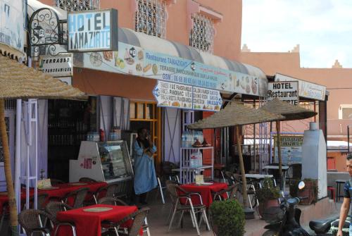 a woman standing in front of a restaurant with tables and umbrellas at Auberge Restaurant Rooftop Tamazirt in Boumalne