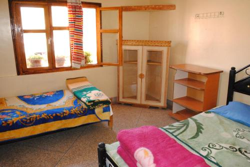a room with two beds and a desk and window at Auberge Restaurant Rooftop Tamazirt in Boumalne