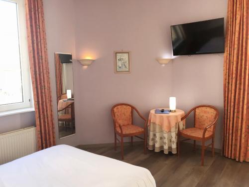 ein Hotelzimmer mit einem Tisch, Stühlen und einem TV in der Unterkunft Hotel Claridge in Blankenberge