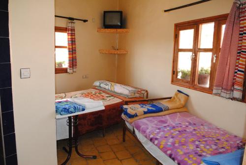 Habitación con 2 camas y TV en la pared. en Auberge Restaurant Rooftop Tamazirt, en Boumalne