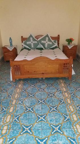 a bedroom with a wooden bed on a blue rug at Écologie oasis tafilalt CHEZ L' HABITANT in Er Rachidia