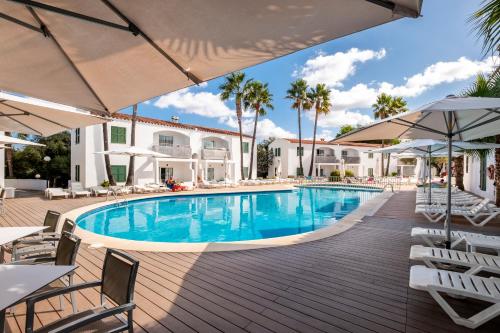 a pool at a resort with chairs and umbrellas at Apartaments Cales de Ponent in Ciutadella