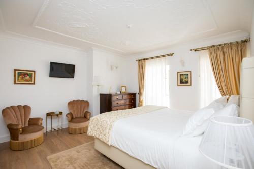 a white bedroom with a bed and two chairs at Sra da Oliveira Solar Heritage in Leiria