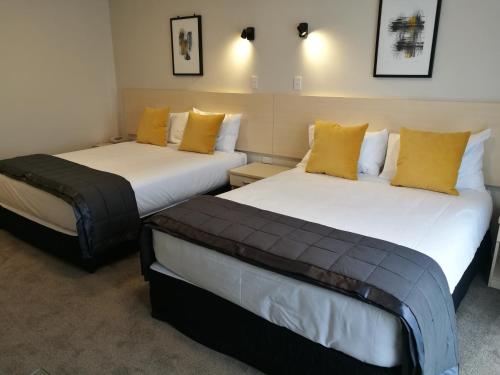 two beds in a room with yellow pillows at The Victoria Hotel Dunedin in Dunedin
