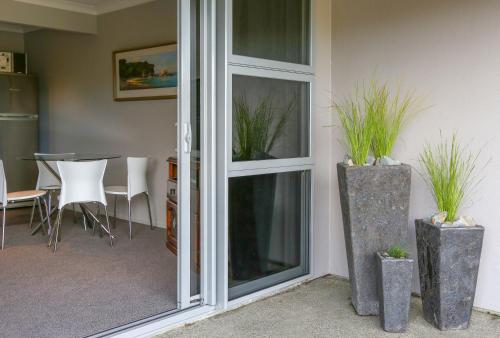 une porte coulissante en verre avec deux plantes en pot à côté d'une table dans l'établissement Two Tuis Accomodation, à Kaiteriteri