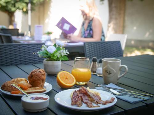 a wooden table with plates of breakfast food and orange juice at Hôtel Inn Design Resto Novo Vannes in Theix