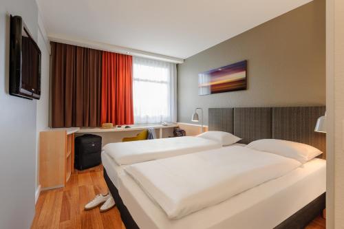 a hotel room with two beds and a desk at ibis Hotel Frankfurt Messe West in Frankfurt/Main