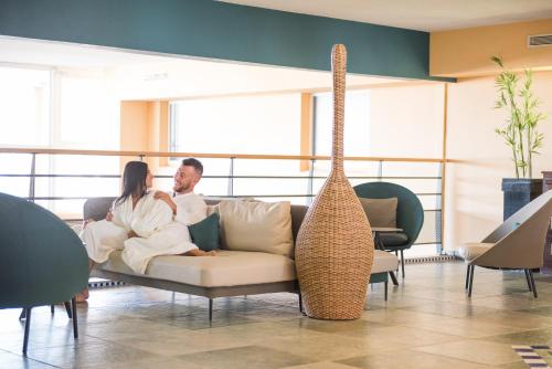 a man and woman sitting on a couch in a room at Grand Hôtel Les Flamants Roses Thalasso & Spa in Canet-en-Roussillon