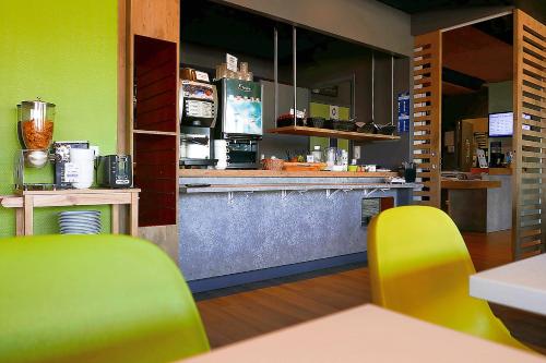 a restaurant with a counter and yellow chairs in a room at Hotel ibis Budget Laval in Bonchamp-lès-Laval