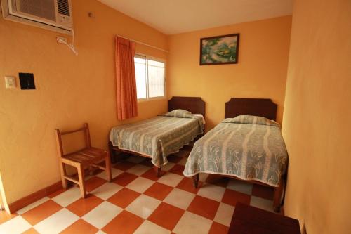 a bedroom with two beds and a chair and a window at Hotel Bugambilias in Ticul