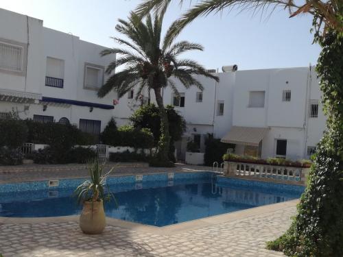 a swimming pool with two palm trees and a building at Sonny Apartment in Hammamet