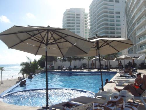 a swimming pool with umbrellas and people sitting on the beach at Ocean Seaview Dream condo next to clubs in Cancún