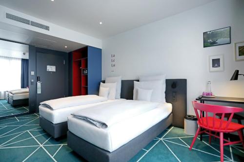 Cette chambre comprend deux lits, un bureau et une chaise rouge. dans l'établissement sander Hotel, à Coblence