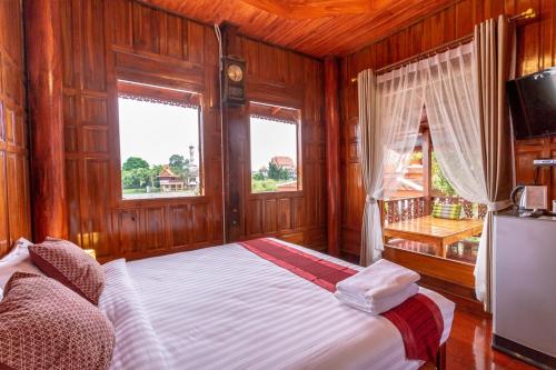 a bedroom with a bed and a television and two windows at Athithara Homestay in Phra Nakhon Si Ayutthaya