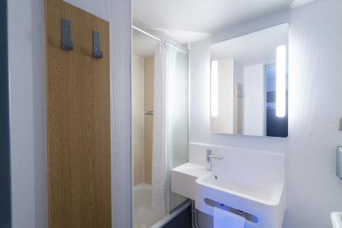een witte badkamer met een wastafel en een spiegel bij B&B HOTEL CHATEAUROUX Aéroport in Déols