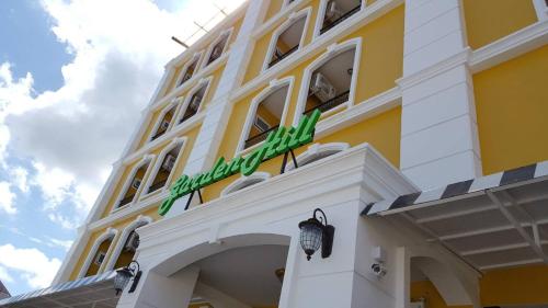 a yellow and white building with a green sign on it at Garden Hill Hotel in Trang