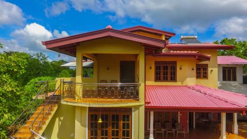 a yellow house with a red roof and a balcony at Sigiriya Peacock Homestay in Sigiriya