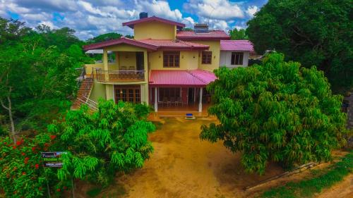 a yellow house with a red roof and trees at Sigiriya Peacock Homestay in Sigiriya