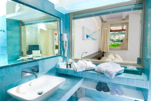 Baño azul con lavabo y espejo en Hotel Punta Est, en Baja Sardinia