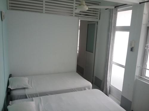 a white bedroom with two beds and a window at La Plaine Verte Guesthouse in Port Louis