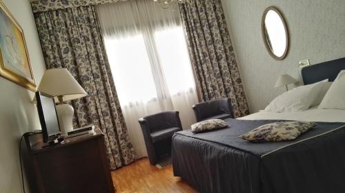 a bedroom with a bed, chair, lamp and a window at Hotel Tosco Romagnolo in Bagno di Romagna