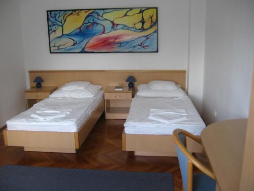 2 Betten in einem Zimmer mit einem Tisch und einem Gemälde in der Unterkunft Leier Business Hotel in Gönyů