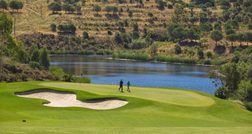 two people standing on a golf course next to a lake at Monte Rei Golf & Country Club in Vila Nova de Cacela