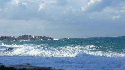 a wave in the ocean with a city in the background at Milner Flats in Sliema