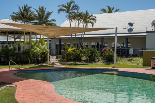 a swimming pool with a tan umbrella in front of a building at Illawong Beach Resort in Mackay