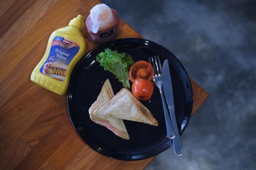 a plate of food with a sandwich and a bottle of mustard at Bed & Bike Hostel in Chiang Rai