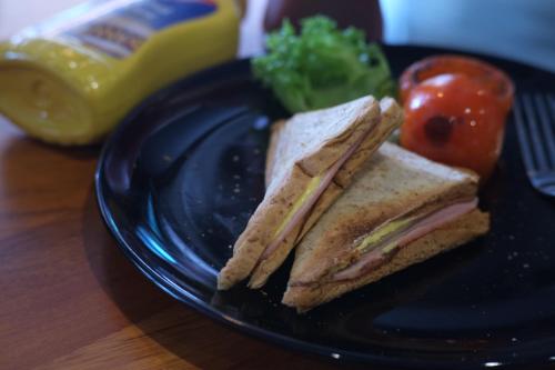 a sandwich on a black plate with a tomato and broccoli at Bed & Bike Hostel in Chiang Rai