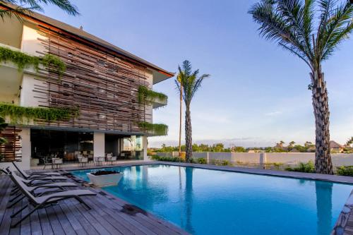 - une piscine avec des chaises et des palmiers à côté d'un bâtiment dans l'établissement The Double View Mansions Bali, à Canggu